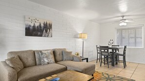 Una sala de estar con un sofá, una mesa de centro, una mesa de comedor con sillas, una lámpara de pie y un ventilador de techo.
