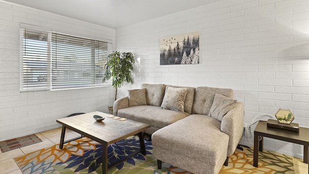 Una sala de estar con un sofá modular, una mesa de centro, una mesita auxiliar, una planta en maceta y un cuadro en la pared.