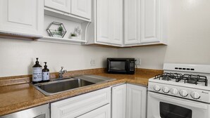 Una cocina con armarios blancos, encimera de granito, pileta de acero inoxidable, microondas negro y cocina a gas blanca.