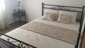 A neatly made bed with a patterned bedspread and two pillows, a small bedside table with a lamp, and a plain wall with a single picture.