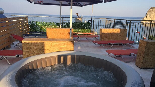 A hot tub surrounded by wooden seating and a view of the sea.