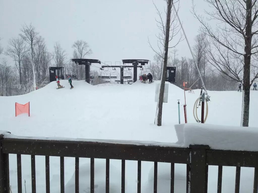 A snow-covered ski lift area with a wooden fence in the foreground.