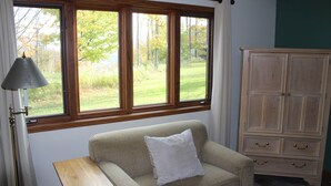 Una habitación con un sofá color beige, un aparador de madera y un ventanal con vistas a una zona verde.