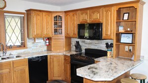 Una cocina con armarios de madera, encimera de granito, estufa, lavavajillas y taburetes de bar.
