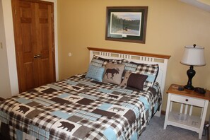 A bedroom with a checkered bedspread, a wooden headboard, a bedside table with a lamp, and a framed picture on the wall.