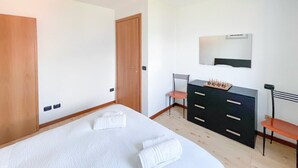 A bedroom with a bed, a dresser, a chair, and a mirror. - BLUE HOUSE 3 by Design Studio (Bellano)
