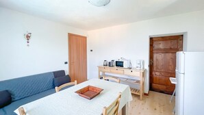A compact living space with a kitchenette, a dining table, and a sofa. - BLUE HOUSE 3 by Design Studio (Bellano)