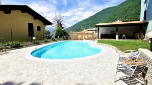 A swimming pool with a tiled deck, outdoor seating, and a mountain backdrop. - BLUE HOUSE 3 by Design Studio (Bellano)