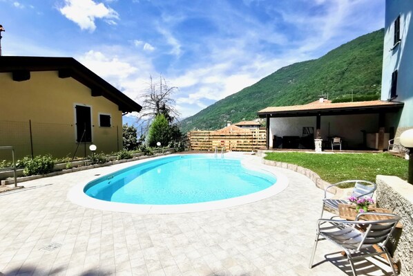 Una piscina con solárium alicatado, mobiliario exterior y montañas al fondo.