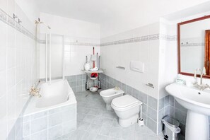Ein modernes Badezimmer mit Badewanne, zwei Toiletten, einem Waschbecken und einer Dusche.