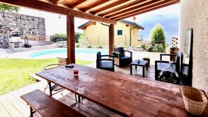 An outdoor patio with wooden tables and chairs, a pool, and a stone wall in the background. - BLUE HOUSE 3 by Design Studio (Bellano)