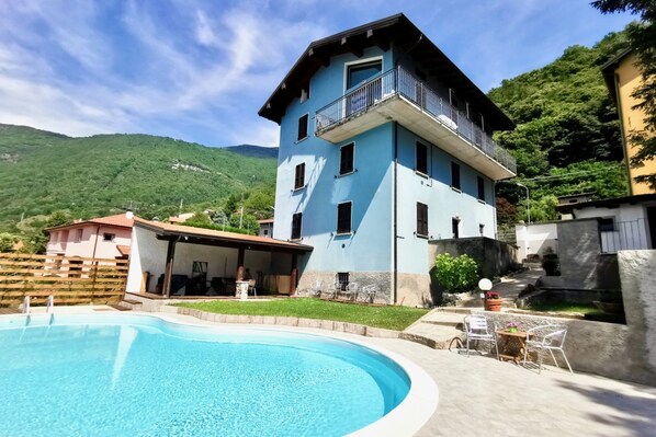 Ein zweistöckiges Gebäude mit Balkon, Schwimmbecken und einer Terrasse mit Gartenmöbeln.