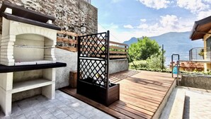 An outdoor kitchen area with a stone oven, a wooden deck, and a view of mountains. - BLUE HOUSE 3 by Design Studio (Bellano)