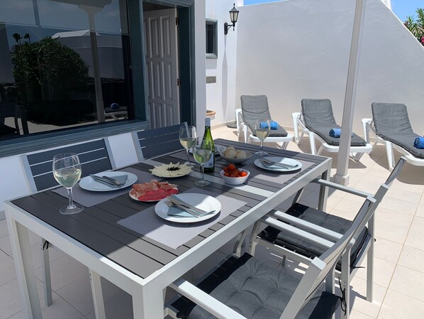 Una mesa de comedor dispuesta con platos, cubiertos y vasos, rodeada de sillones.