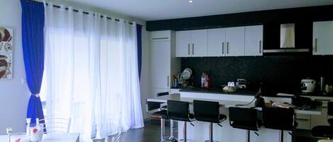 A modern kitchen with white cabinets, a black countertop, and three bar stools.