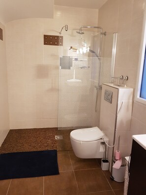 Uma casa de banho moderna com chuveiro, sanita e uma pequena área de lavatório.
