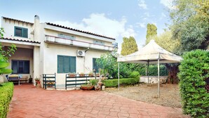 A two-story house with a paved patio, a covered outdoor seating area, and a garden with various plants and a tree. - Villetta Gina (Avola)