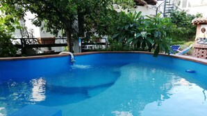 A swimming pool with clear blue water, surrounded by greenery and a tiled deck. - Villetta Gina (Avola)