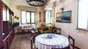 A dining area with a round table, chairs, a green sofa, and a painting on the wall. - Villetta Gina (Avola)