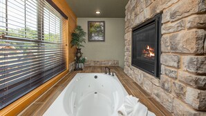 Un área de spa con una bañera grande, paredes de piedra, chimenea y una ventana con persianas.