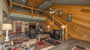 A spacious living room with a high ceiling, wooden beams, a staircase, and a kitchen in the background. - Bearvue Point (Gatlinburg)