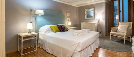 Ein Schlafzimmer mit einem großen Bett, Nachttischen, einer Kommode, einem Sessel und einem großen Fenster.