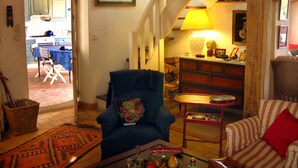 Ein Wohnzimmer mit blauem Sessel, einem gestreiften Sofa, einem Essbereich mit Tisch und Stühlen und einer Treppe, die zu einer oberen Ebene führt.