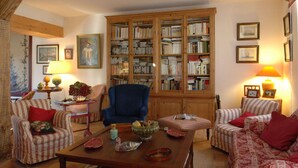 Ein gemütliches Wohnzimmer mit gestreiften Sofas, einem hölzernen Bücherregal und einem blauen Sessel.