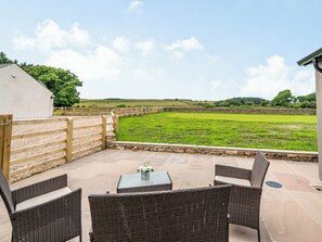 An outdoor patio with wicker furniture, a table, and a view of a green field.