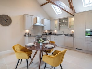 A modern kitchen with white cabinetry, a wooden dining table with yellow chairs, and a skylight above.