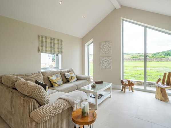 A spacious living room with a large window, a sofa, a coffee table, and a view of the countryside.