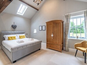 A bedroom with a large bed, a wardrobe, a chair, and a window with curtains.