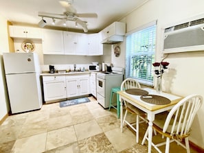 A kitchen with white cabinets, a refrigerator, a microwave, and an oven. There is a window with blinds and a vase with flowers on the counter.