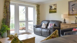 A living room with a leather sofa, a wooden coffee table, and a dining table with a bowl and candles. There are curtains, a painting, and a lamp on a side table. - 3 bedroom accommodation in Bampton, near Tiverton (Bampton, near Tiverton)