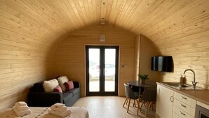 A cozy, wooden-paneled room with a bed, a small desk, a chair, a TV, and a sink.