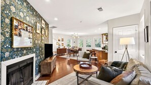 A spacious living room with a fireplace, a dining area, and a kitchen in the background. - Stylish Inman Park Condo, Walk to Beltline (Atlanta)