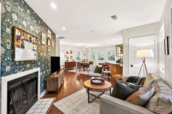A spacious living room with a fireplace, a dining area, and a kitchen in the background.