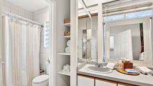 A bathroom with a shower, toilet, vanity with a mirror, and shelves with towels. - Stylish Inman Park Condo, Walk to Beltline (Atlanta)