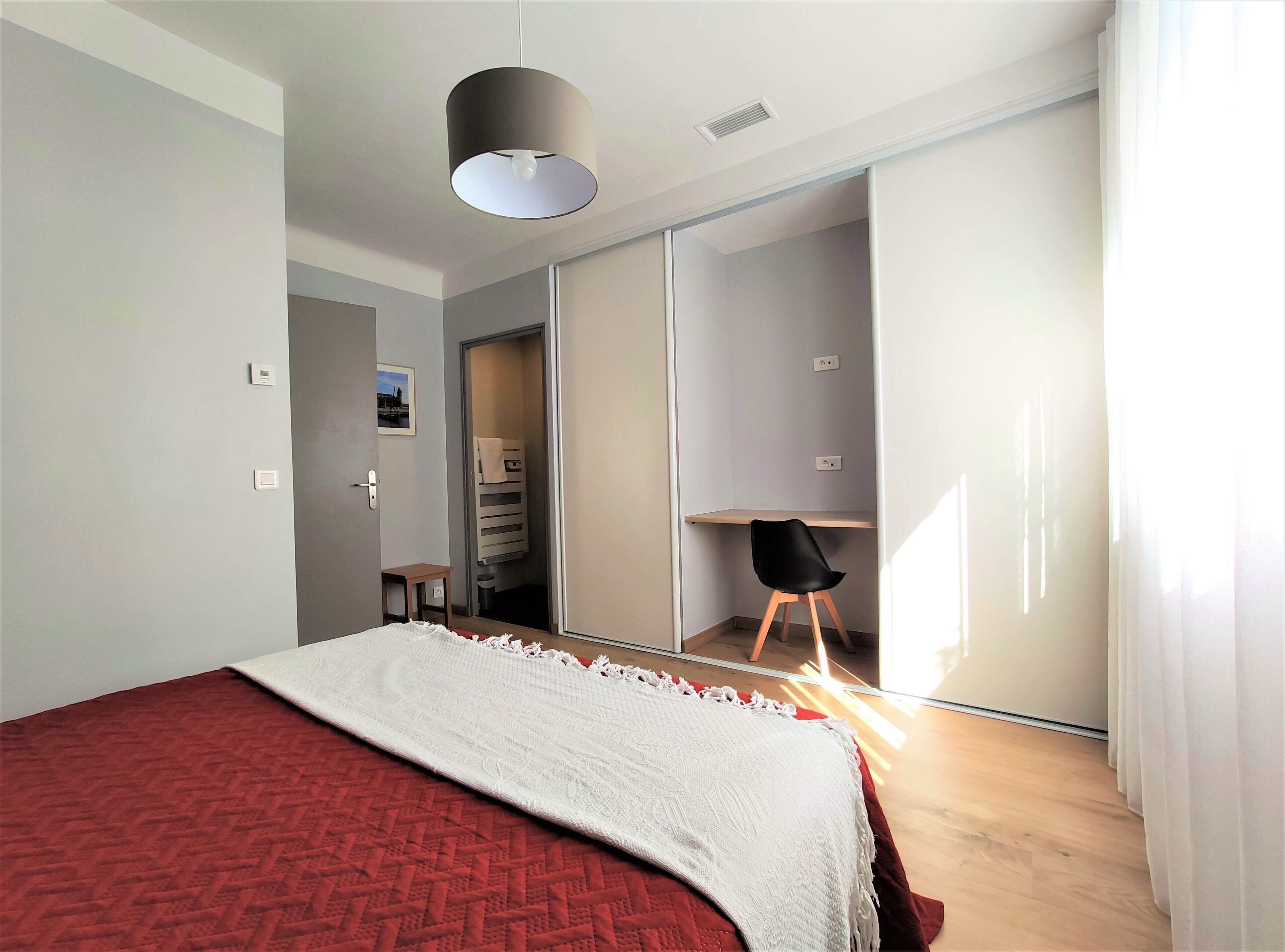 A bedroom with a bed, a desk, a chair, a wardrobe, and a mirror.