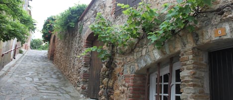 A narrow stone-paved street flanked by old buildings with wooden shutters and a number '8' sign.
