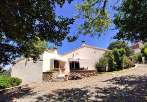 Uma casa com fachada de pedra, um pátio com móveis de exterior e um céu azul claro.