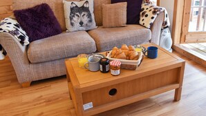 A cozy living room with a sofa, pillows, a coffee table with breakfast items, and a wooden shelf with decorative items.