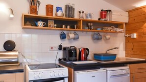A compact kitchen with a stove, oven, and dishwasher. There are shelves above the counter holding various kitchen items.