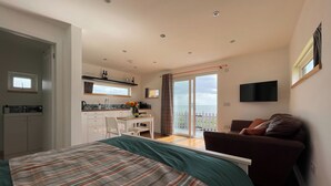A bedroom with a bed, a sofa, a TV, a kitchen area, and a balcony with a view. - 1 bedroom accommodation in Hilton, near Tain (Hilton, near Tain)