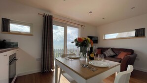 A dining area with a table set for two, a sofa, and a view of the sea. - 1 bedroom accommodation in Hilton, near Tain (Hilton, near Tain)