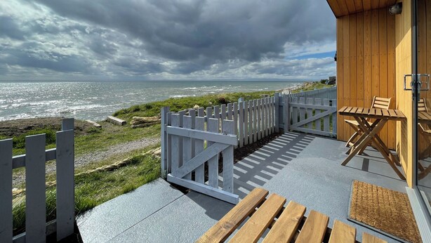 A wooden deck with a view of the sea, a white fence, and a table with chairs. - 1 bedroom accommodation in Hilton, near Tain (Hilton, near Tain)