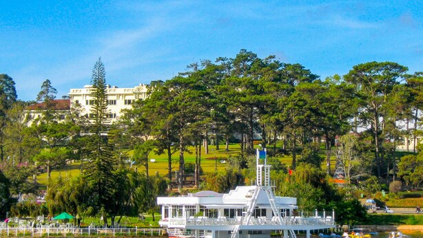 A white building with a tower, surrounded by lush green trees and a clear blue sky.