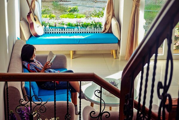 A person sitting on a sofa with a guitar leaning against the wall, reading a book.