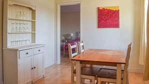 Un comedor con una mesa y sillas de madera, un armario blanco con cristalería, y una puerta que da a otra habitación.