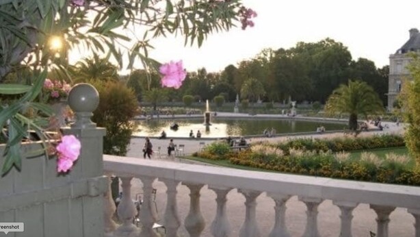 Blick auf einen Garten mit einem Brunnen, Bänken und Menschen, die dort spazieren.